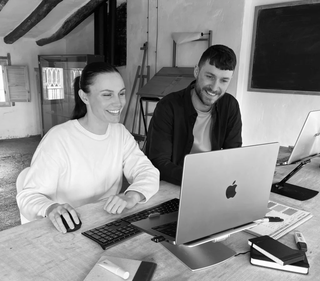 The two founders of Vaughan&Mont sat at a desk smiling whilst working on their web design business